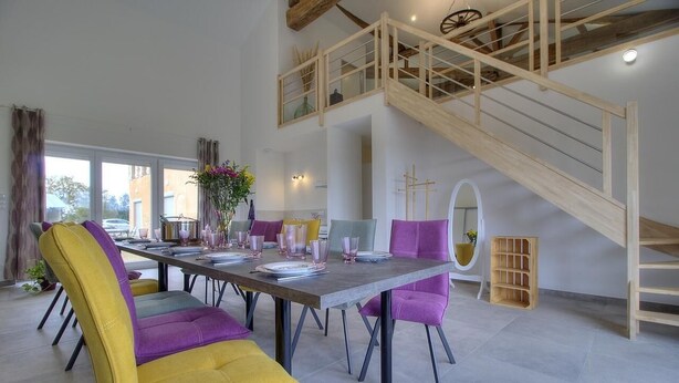 A dining area with a high wooden staircase, a dining table set with plates and glasses, and colorful chairs. - Champ Clair - SAINT BENIGNE (SAINT BENIGNE)