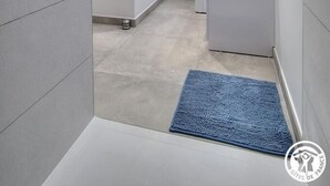 Ein schmaler Flur mit einer blauen Matte am Eingang, einer weißen Tür und einem weißen Heizkörper im Hintergrund.