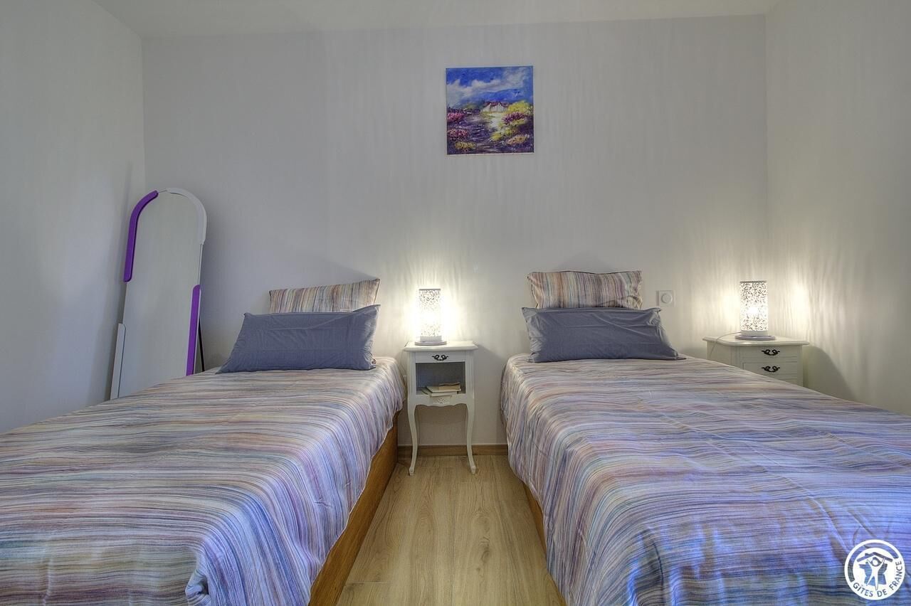 Une chambre avec deux lits, une table de chevet avec une lampe et une planche de surf appuyée contre le mur.