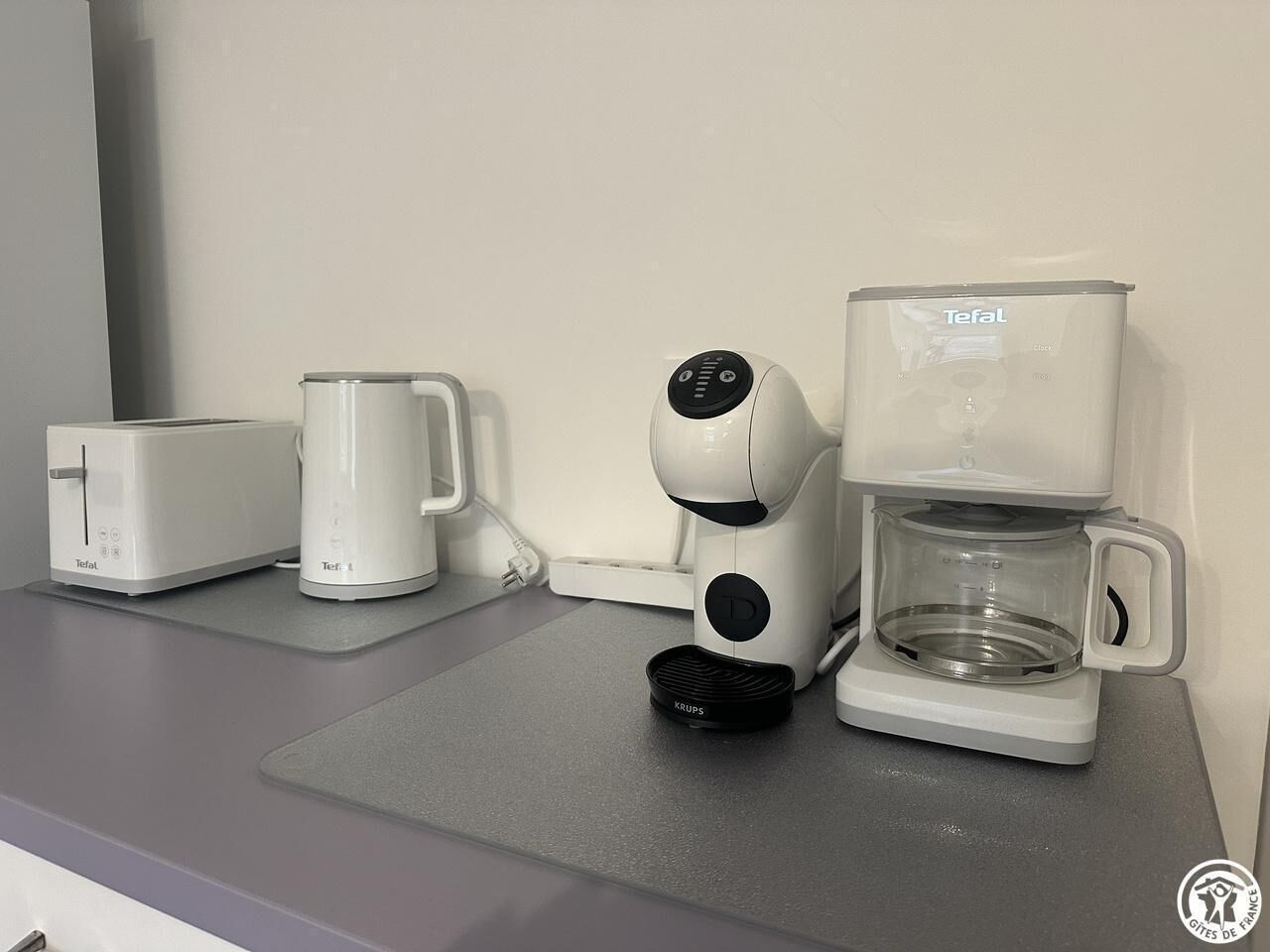 Een aanrecht met een Toffel broodrooster, een Krups koffiezetapparaat en een glazen koffiekan.