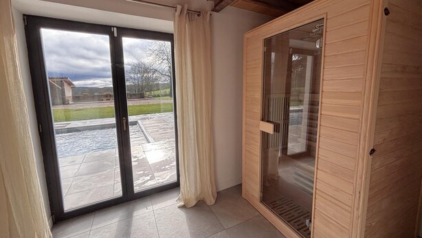 Une pièce dotée d’une porte-fenêtre coulissante donnant sur un patio, d’un sauna en bois et d’un sol carrelé.