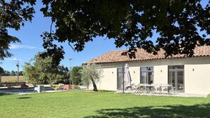 Un bâtiment avec un toit en tuiles, une terrasse avec des tables et des chaises, et une pelouse verdoyante.