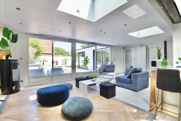 A modern living room with a large glass door leading to an outdoor area, a sofa, ottomans, and a coffee table.