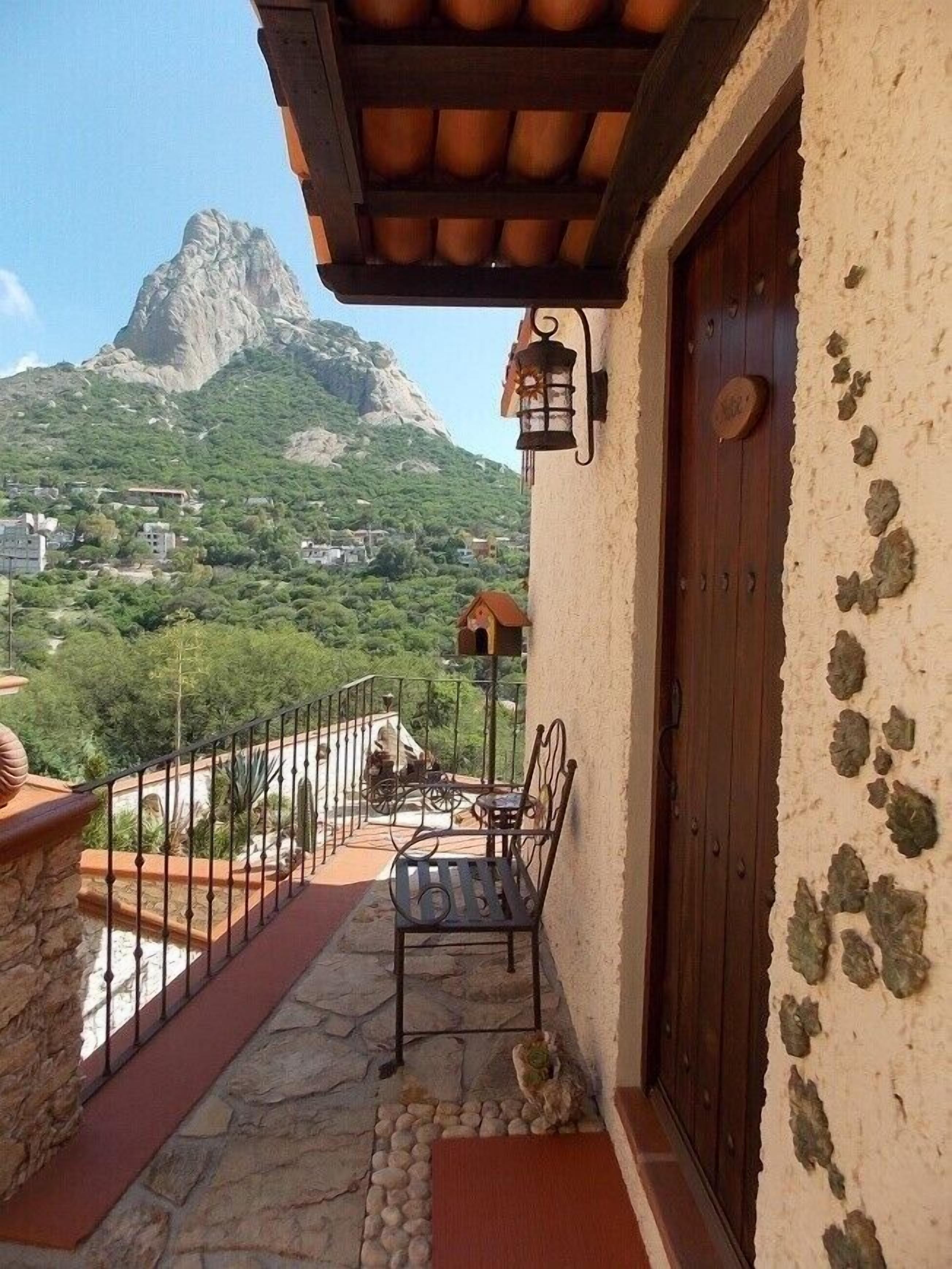 A balcony with a stone floor, a metal railing, a wooden door, and a view of a mountain.