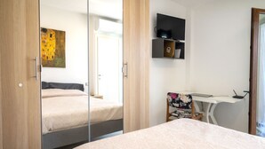 Un dormitorio con cama, escritorio con silla, televisor y un cuadro en la pared.