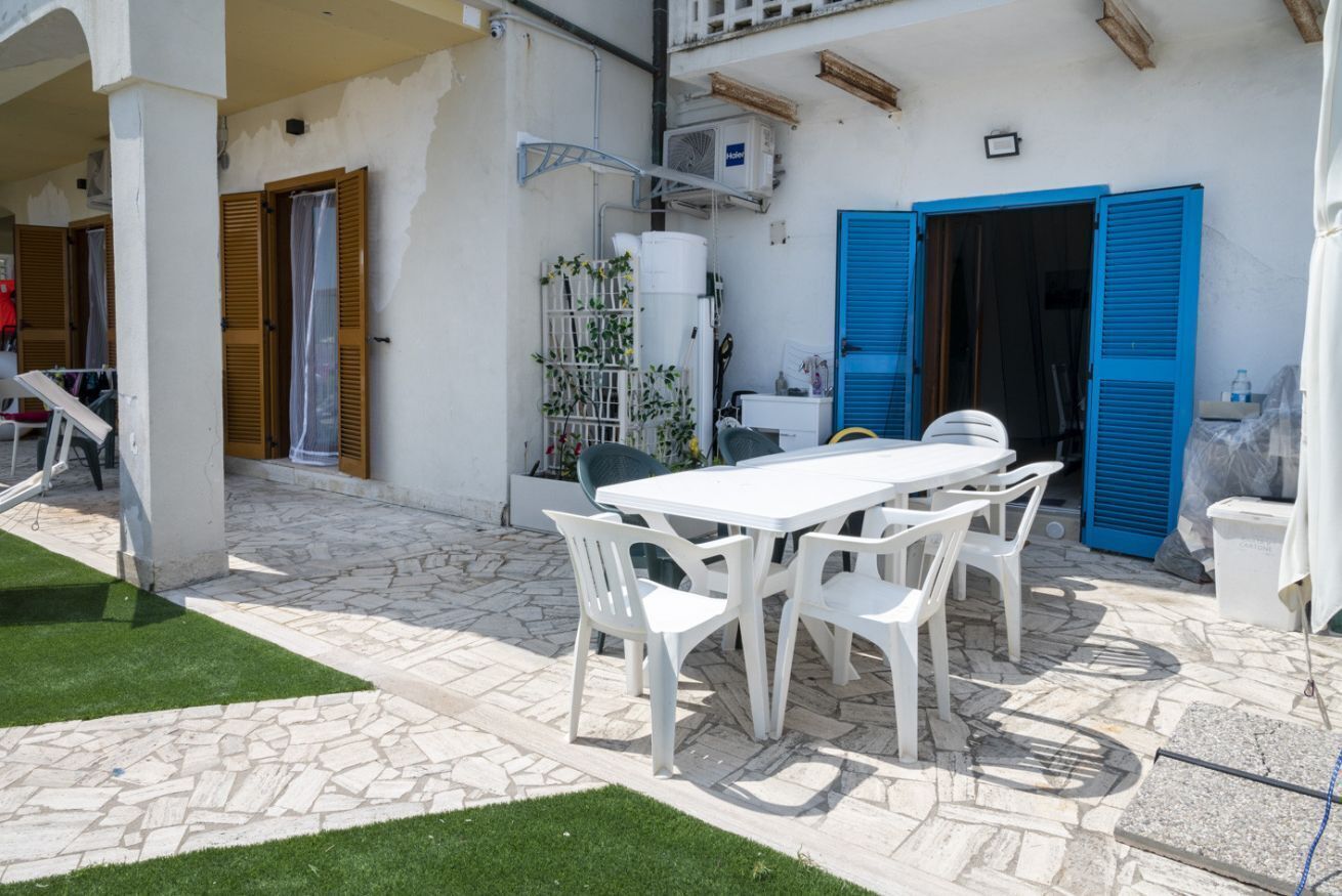 A patio with a white table and chairs, a water tank, and blue shutters on a building.