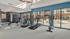 Une salle de sport moderne équipée de tapis de course, de vélos d’appartement et d’autres appareils d’exercice. De grandes fenêtres offrent une vue sur l’extérieur.