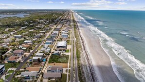 An aerial view of a coastal residential area with houses, a beach, and a pier.