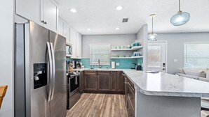 A modern kitchen with a stainless steel refrigerator, wooden cabinets, a marble island, and pendant lighting.