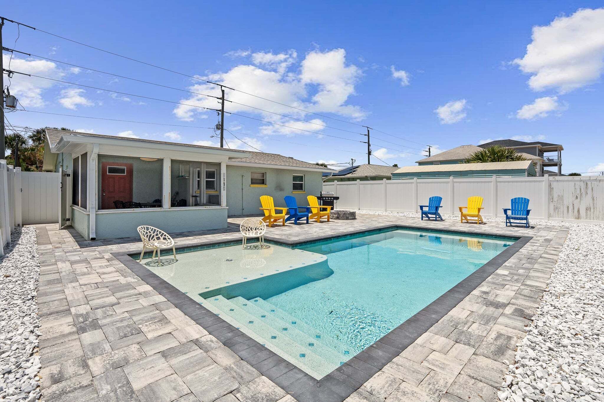 A swimming pool with a tiled deck, a small building, and several colorful chairs.