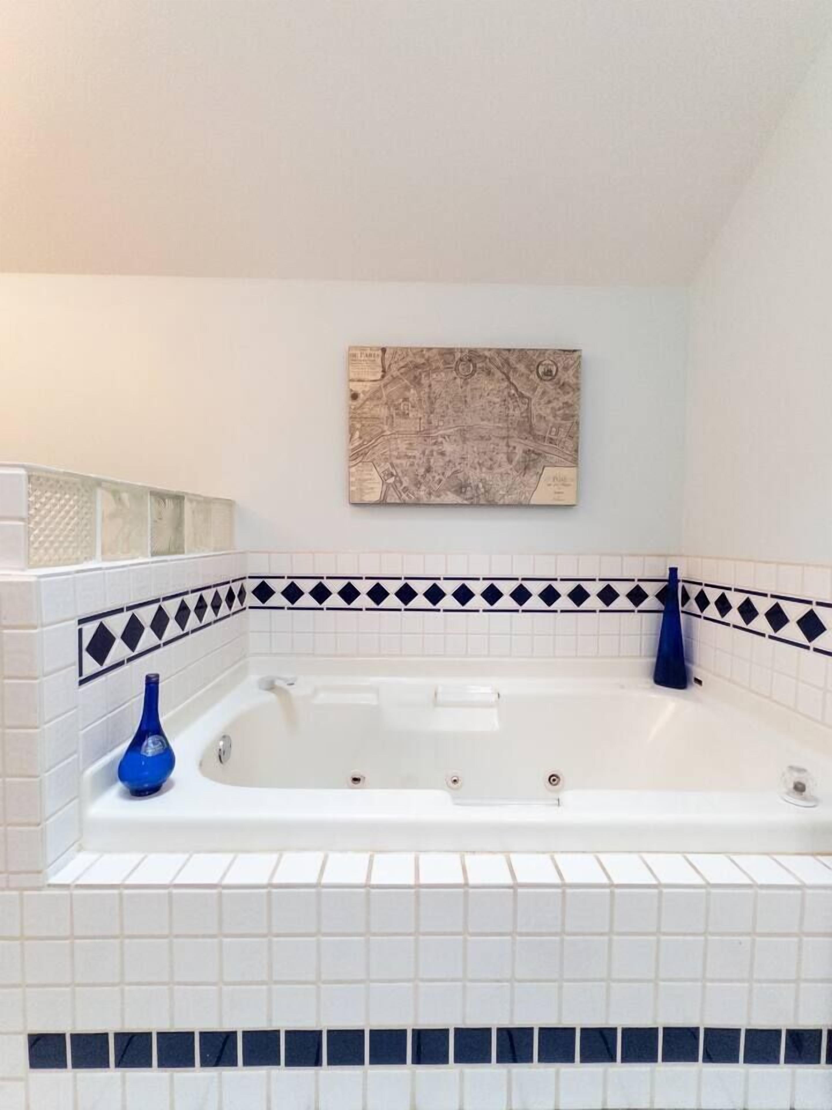 Une salle de bain avec une baignoire blanche, des carreaux décoratifs bleus et une œuvre d’art représentant une carte géographique accrochée au mur.