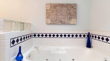 A bathroom with a white bathtub, blue decorative tiles, and a map artwork on the wall.