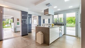 A modern kitchen with a central island, a dining area with chairs, and a view of a garden through the glass door. - Amazing home in Santa Eulalia des Riu (Santa Eulalia des Riu)