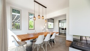 A modern kitchen with a wooden island, white chairs, pendant lights, and large windows. - Amazing home in Santa Eulalia des Riu (Santa Eulalia des Riu)