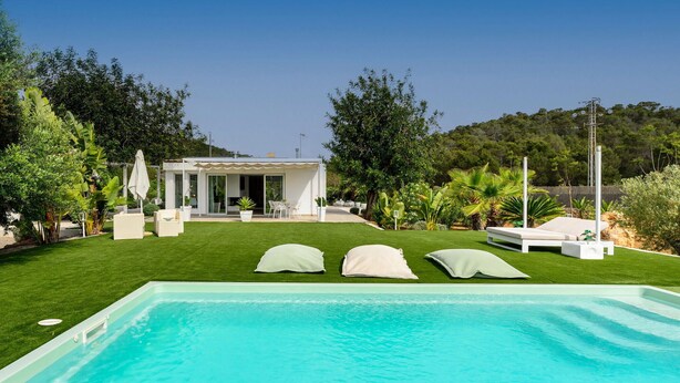 A pool area with three white lounge chairs and a covered patio with outdoor furniture. - Amazing home in Santa Eulalia des Riu (Santa Eulalia des Riu)