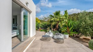 A modern house with a glass door leading to a bedroom, a patio with outdoor seating, and a lush garden with various plants. - Amazing home in Santa Eulalia des Riu (Santa Eulalia des Riu)