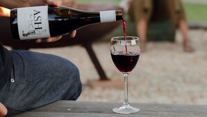 Una persona sirve vino en una copa sobre un banco de madera.
