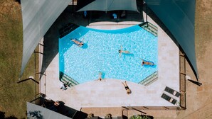 Vista aerea di una piscina con quattro persone a nuoto, circondata da una zona prendisole coperta.
