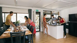 Una cucina moderna con isola centrale, un'area pranzo con tavoli in legno e vista all'esterno tramite ampie finestre.