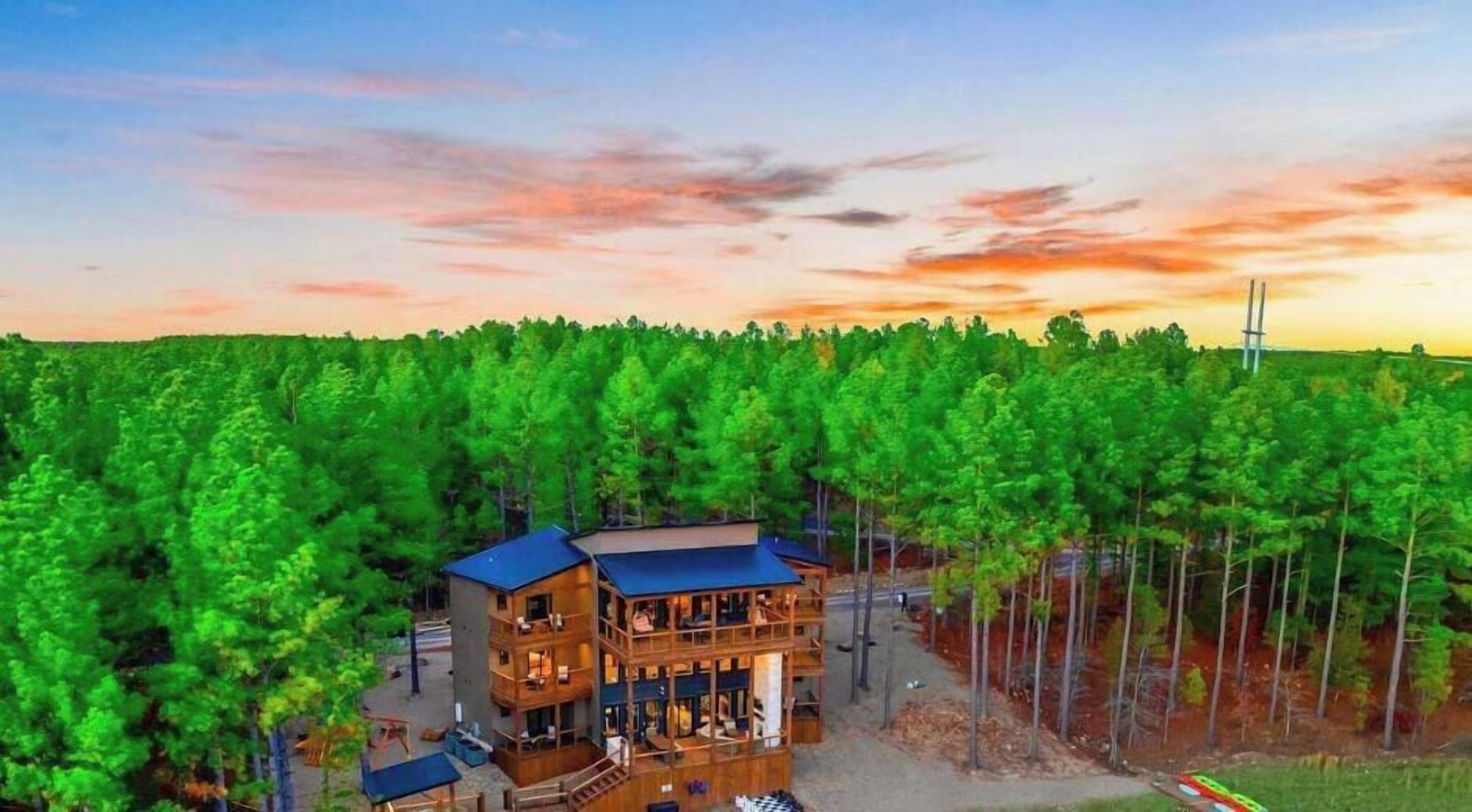 A multi-story wooden cabin with a balcony, surrounded by dense forest.