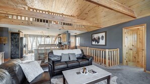 Ein großzügiger Wohnbereich mit hoher Holzbalkendecke, einem schwarzen Ledersofa, einem weißen Couchtisch und einem grauen Teppich.
