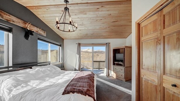 Ein Schlafzimmer mit einem großen Bett, einer Holzbalkendecke, einem aufgehängten Tierkopf und Blick auf Berge durch ein Fenster.