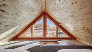 Ein schrägwangiges Schlafzimmer im Dachgeschoss mit großen Fenstern, Holzbalkendecke und zwei Betten.