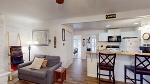 A compact living space with a kitchenette, a gray sofa, wooden chairs, and a small table. - Close to Slopes | WIFI | Pet Friendly | Pinetree 214 (Angel Fire)