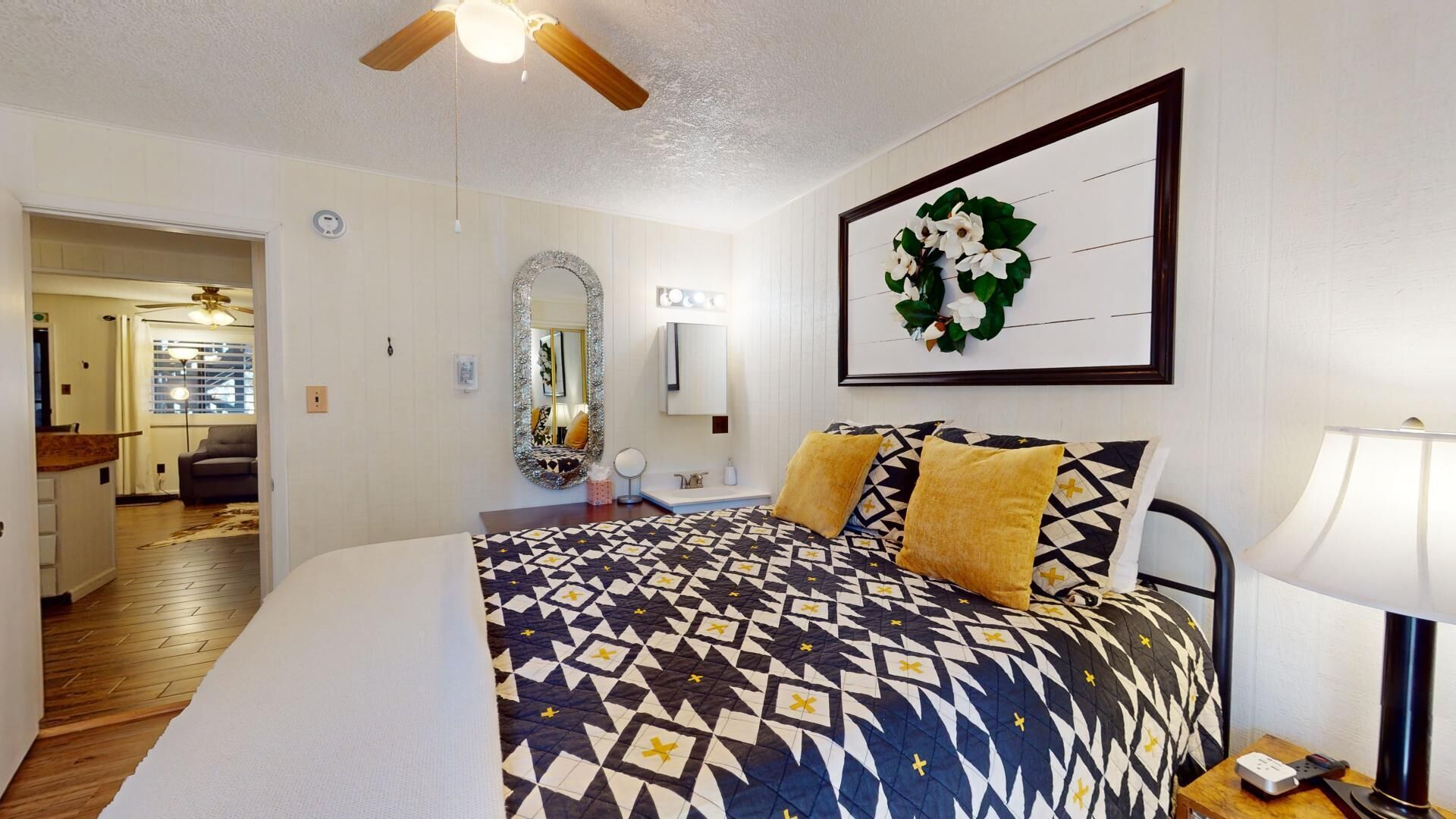 A bedroom with a patterned bedspread, a ceiling fan, a framed picture, and a nightstand with a lamp.