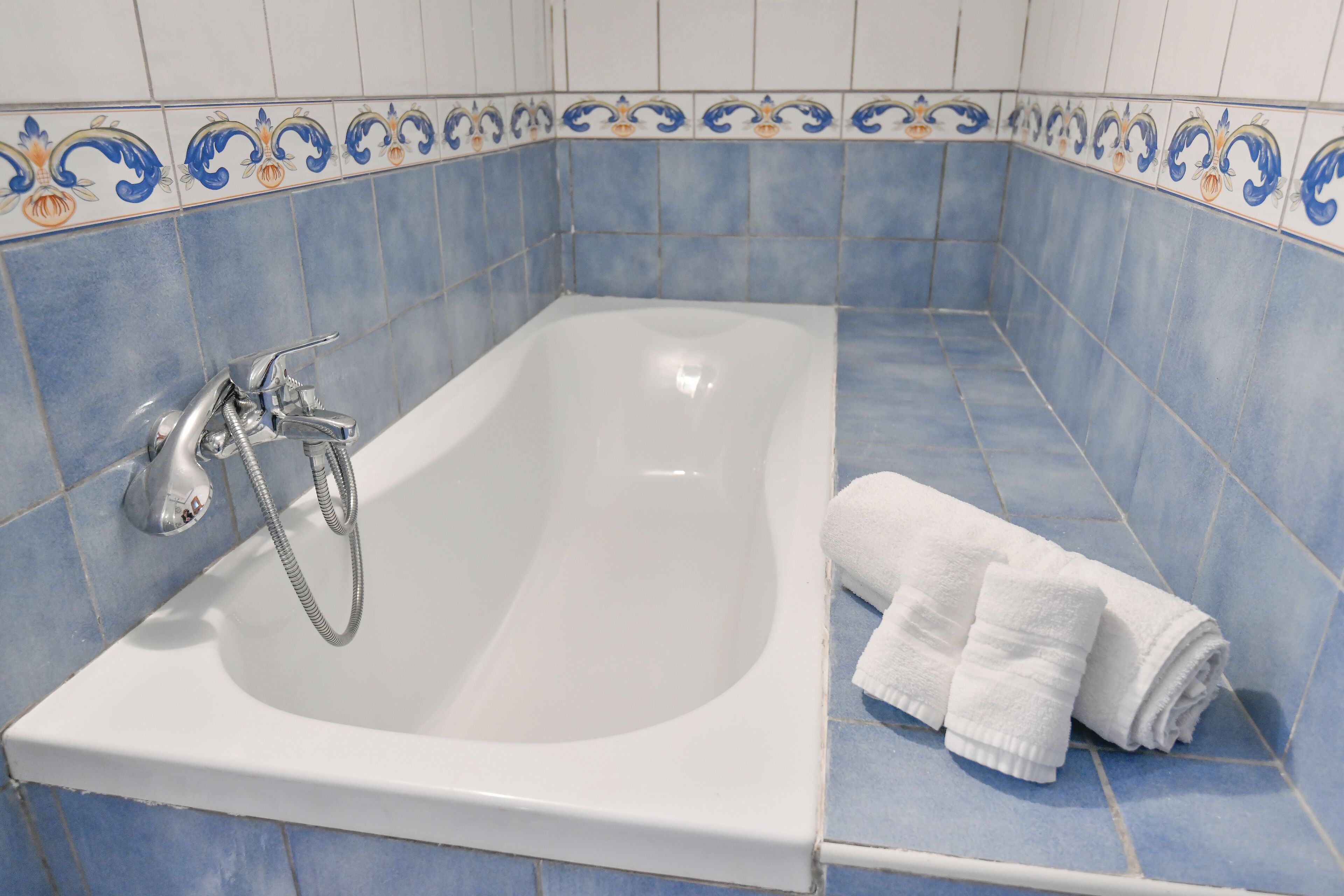 Un baño con una bañera blanca, azulejos azules y un detalle decorativo.