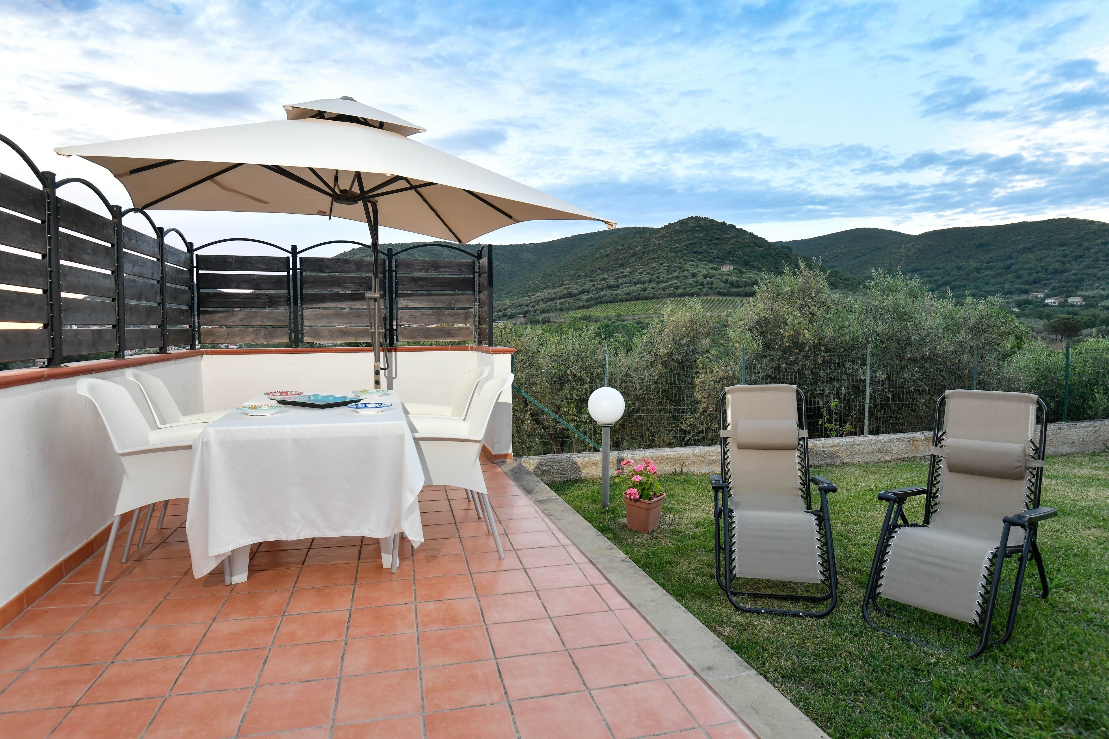 Un patio al aire libre con una mesa blanca, sillas y un paraguas grande.