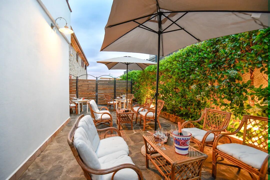 Una terrazza esterna con mobili in vimini, ombrelloni e un muro ricoperto di vegetazione.