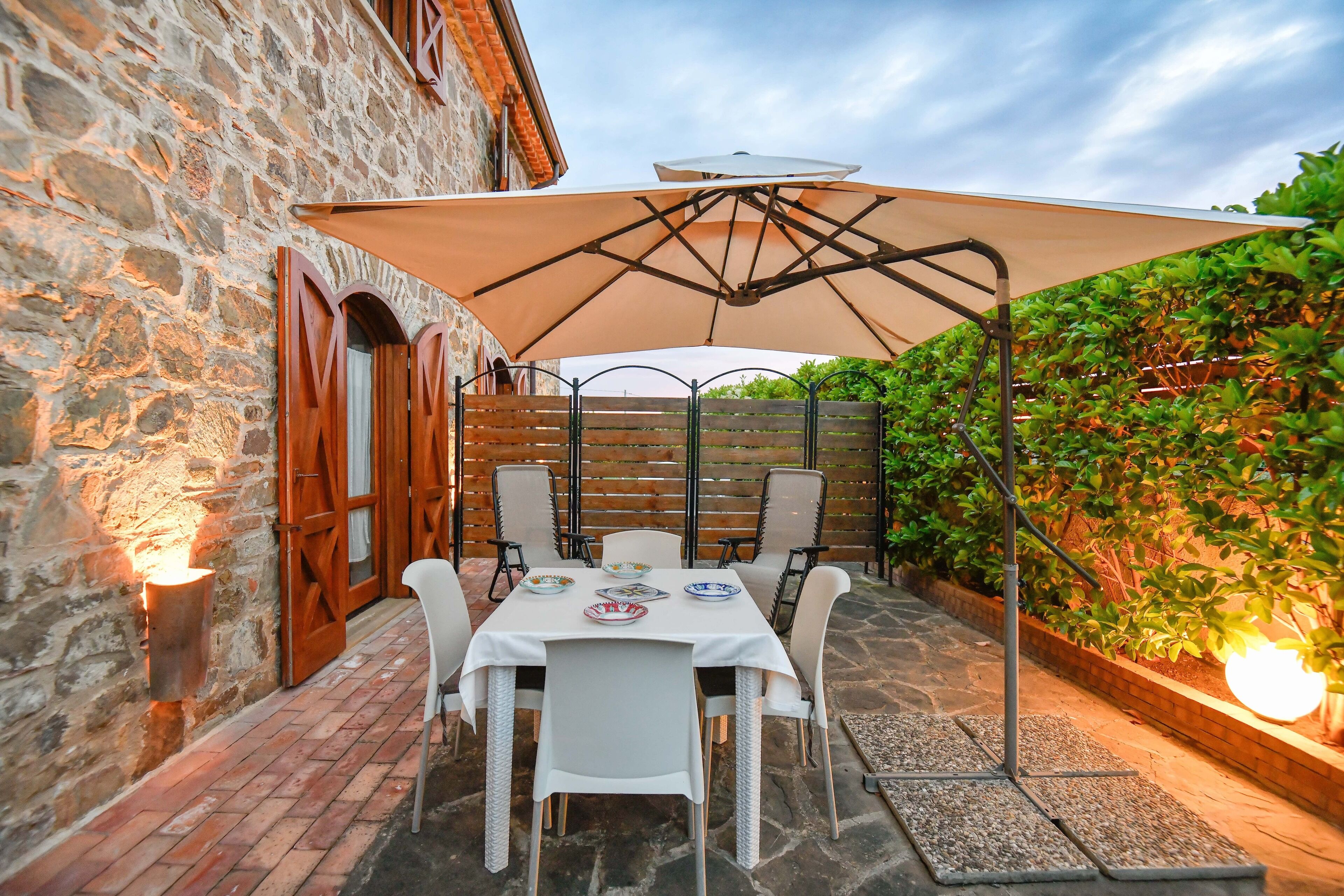 An outdoor patio with a table set for dining, surrounded by stone walls and a wooden fence.