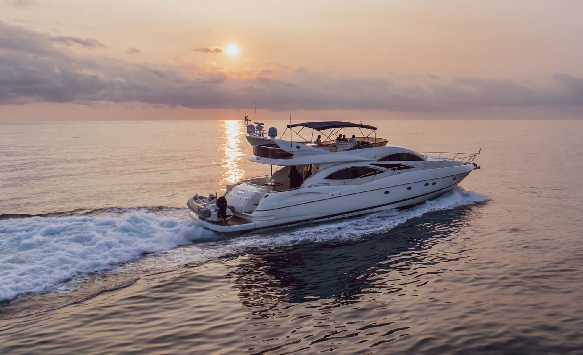 A white yacht with a covered upper deck, moving through calm waters at sunset.