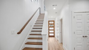 Un escalier avec des marches en bois et des murs blancs, menant à une porte dotée d’un panneau en verre dépoli.