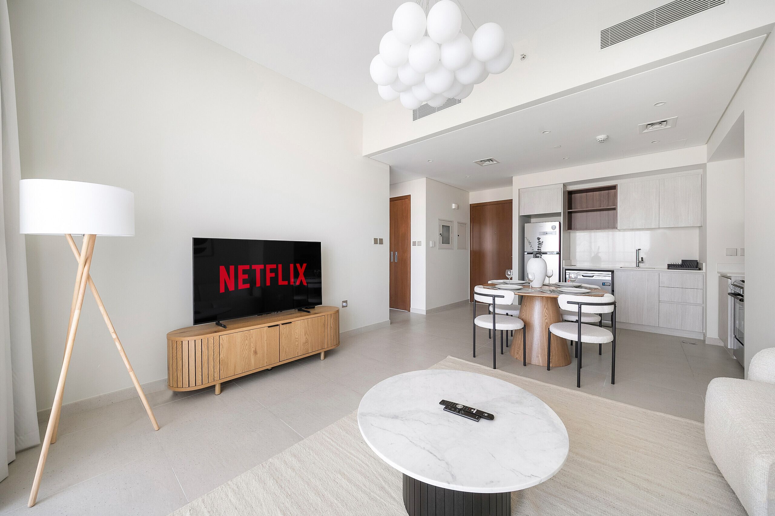 Un soggiorno moderno con televisione a schermo piatto, un tavolino rotondo e una zona pranzo con una piccola cucina sullo sfondo.