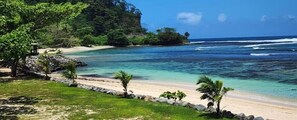 A beach with clear turquoise water, a sandy shore, and lush greenery.