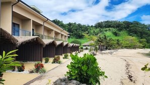 Een resort met rieten daken, een zandstrand en weelderige begroeiing op de achtergrond.