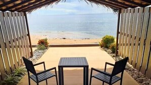 Een overdekt terras met een tafel en stoelen, met uitzicht op een strand.