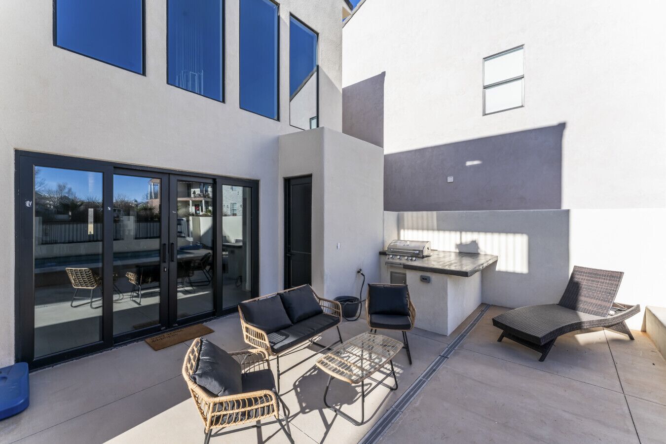 A modern outdoor patio with wicker furniture, a grill, and a sliding glass door leading to a backyard.