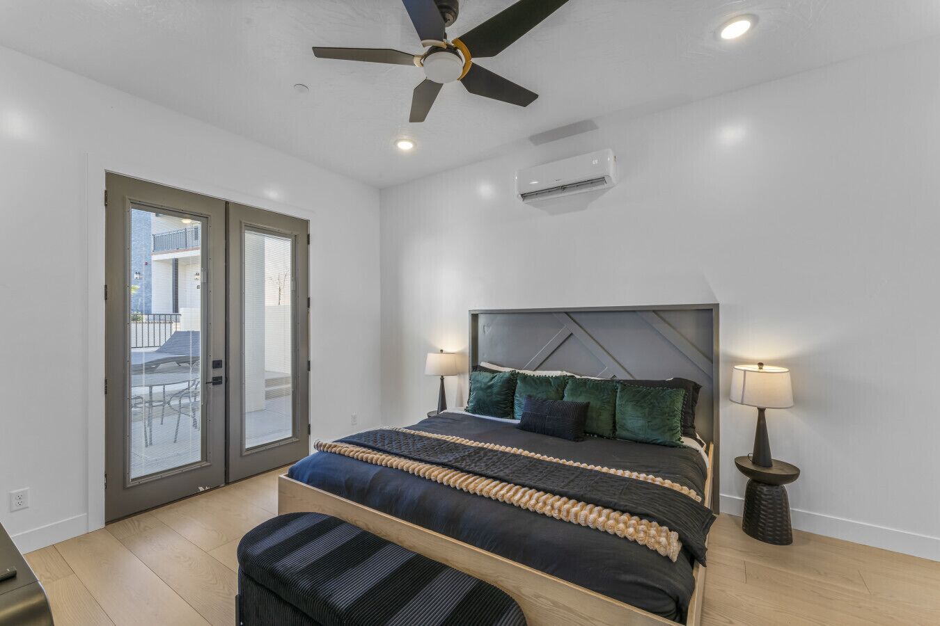 A bedroom with a bed, bedside lamps, a ceiling fan, and an air conditioning unit.
