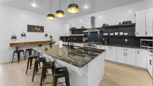 Eine moderne Küche mit einer zentralen Kochinsel, Barhocker, Pendelleuchten und einer schwarzen Spritzschutzwand.