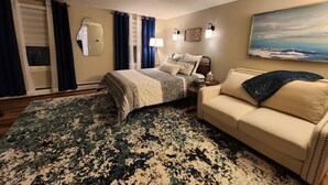 A bedroom with a bed, a sofa, a large rug, a painting, and a window with curtains.