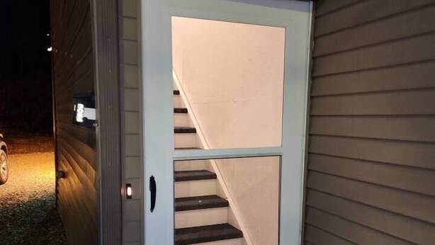 A small, enclosed structure with a door, a visible staircase inside, and a light source outside.