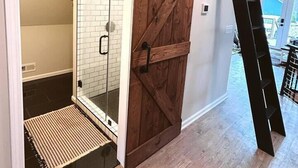A room with a sliding barn door leading to a bathroom with a glass shower enclosure and a wooden floor.