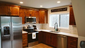 A kitchen with wooden cabinets, stainless steel appliances, a window with a view, and a sign above the window.