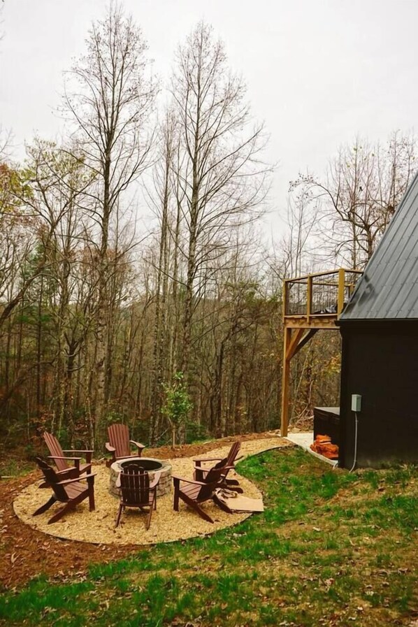 Un jardin avec un foyer, quatre chaises Adirondack et une terrasse en bois.
