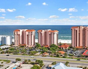 A coastal residential area with high-rise buildings, a beach, and a road with parked cars. - Seachase 1105W | Beachfront | Splash Pad, Pools, Saunas, Hot Tub | My Beach Getaways (Orange Beach)
