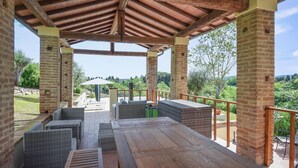 A covered outdoor seating area with wicker furniture and a wooden table, surrounded by brick pillars and a metal railing. - Cozy home in Fauglia with WiFi (Fauglia)