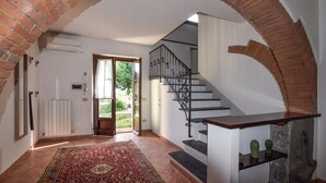 A hallway with a tiled floor, a patterned rug, a staircase with a metal railing, and a brick archway. - Cozy home in Fauglia with WiFi (Fauglia)